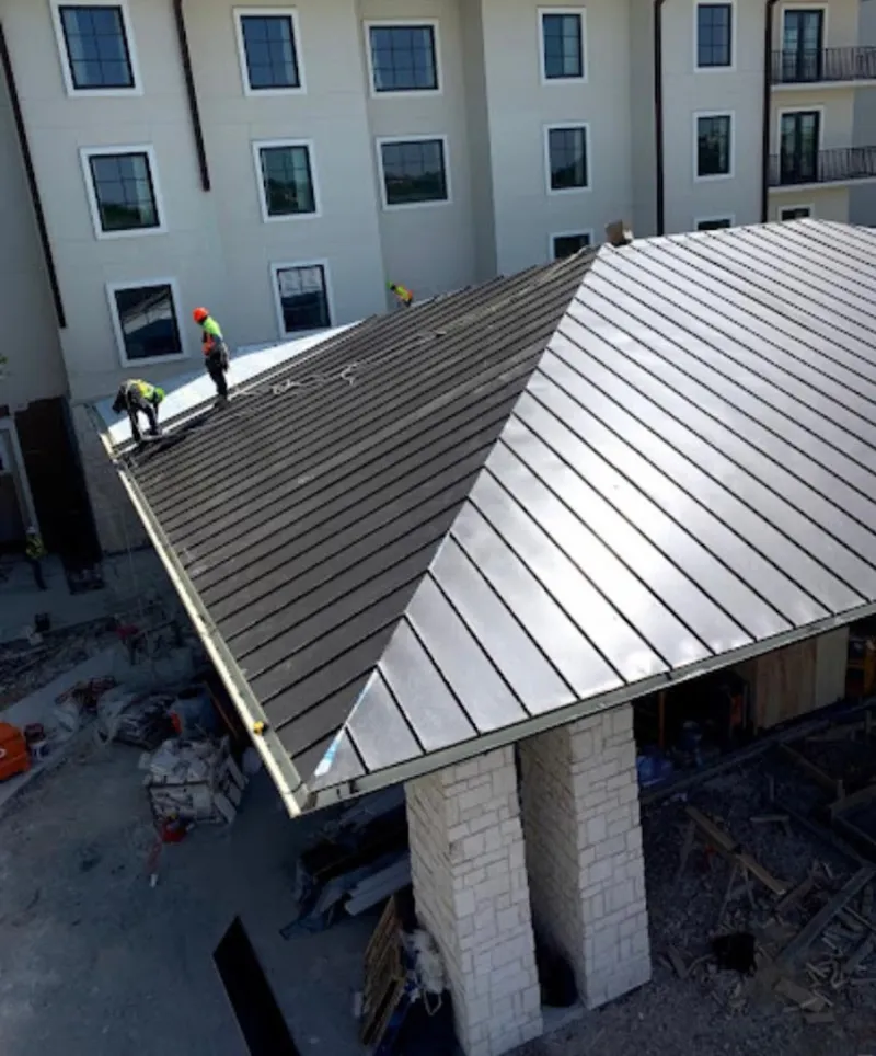 Crew installing standing seam metal roof panels on a commercial project in Independence